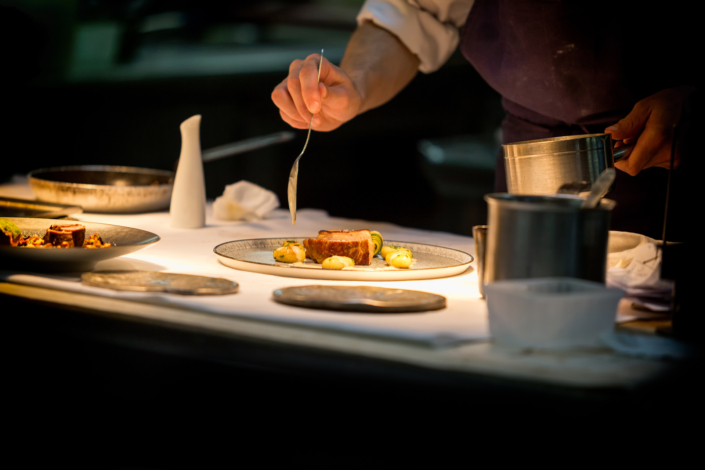 Un chef cuisinier en pleine préparation d'un plat gastronomique sophistiqué, utilisant des ingrédients frais et locaux, illustrant l'engagement de Bevanar & Dorga envers la qualité des produits pour les professionnels de la restauration.