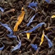 Eine Nahaufnahme von schwarzen Teeblättern, die mit getrockneten Blütenblättern gemischt sind.
Die Teeblätter sind dunkel und gedreht, während strahlend blaue und gelbe Blütenblätter in der Mischung verstreut sind, wodurch ein natürlicher und attraktiver Farbkontrast entsteht.