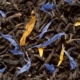 Eine Nahaufnahme von schwarzen Teeblättern, die mit getrockneten Blütenblättern gemischt sind.
Die Teeblätter sind dunkel und gedreht, während strahlend blaue und gelbe Blütenblätter in der Mischung verstreut sind, wodurch ein natürlicher und attraktiver Farbkontrast entsteht.