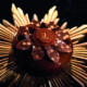 Ein aufwendiges Dessert von 'Etienne Leroy' ist mit einer wunderschönen Schokoladenblume verziert, deren Blütenblätter mit zarten Blumenmotiven geschmückt sind.
Die Blütenblätter sind fächerförmig um die Mitte der Blume angeordnet, wo das Logo der Marke auf einer Schokoladenscheibe zu sehen ist.
Das Dessert steht auf einem goldenen Ständer, der die luxuriöse und elegante Präsentation unterstreicht, die an Raffinesse und Kreativität der Konditoren erinnert.