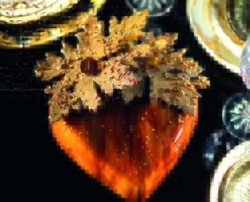 Un dessert en forme de cœur, recouvert d'un glaçage marbré aux teintes orangées et dorées, est décoré de feuilles en chocolat texturées et dorées, disposées avec soin sur le dessus.